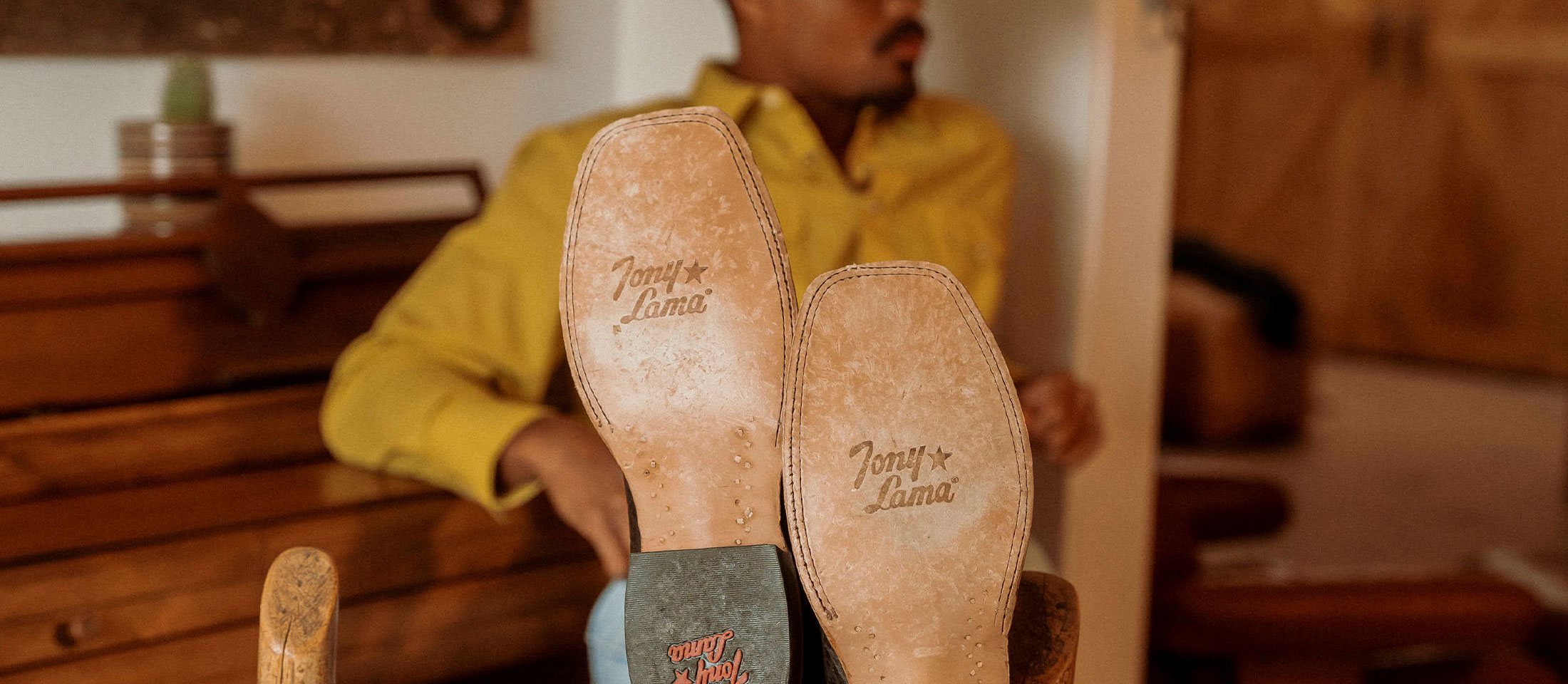 A Cowboy Leaning Against a Piano Bench Wearing the Sealy 13" Western Boots in Brown